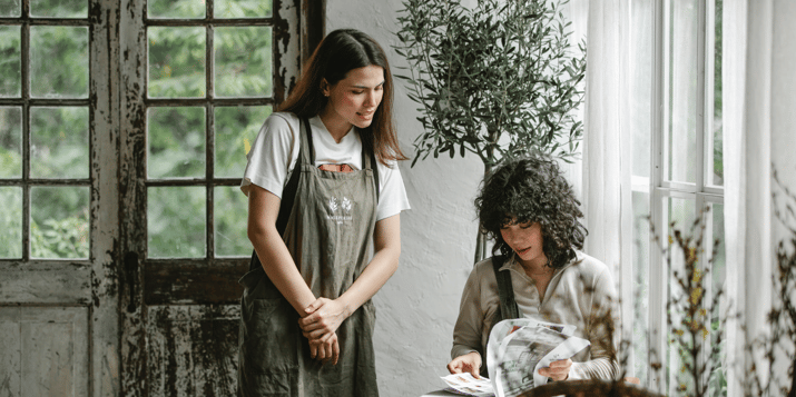 Two women, one wearing an apron and the other sat at a table looking through a menu.