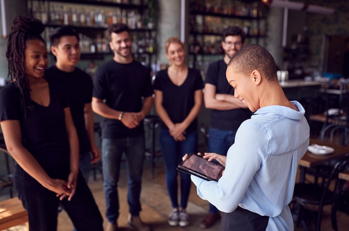 Female restaurant manager talking to five of her staff.