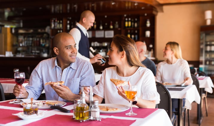 A male and female couple eating pizza at a restaurant.