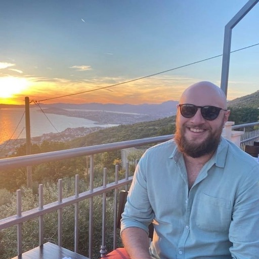 Matt sat on a balcony with a sunset in the background.